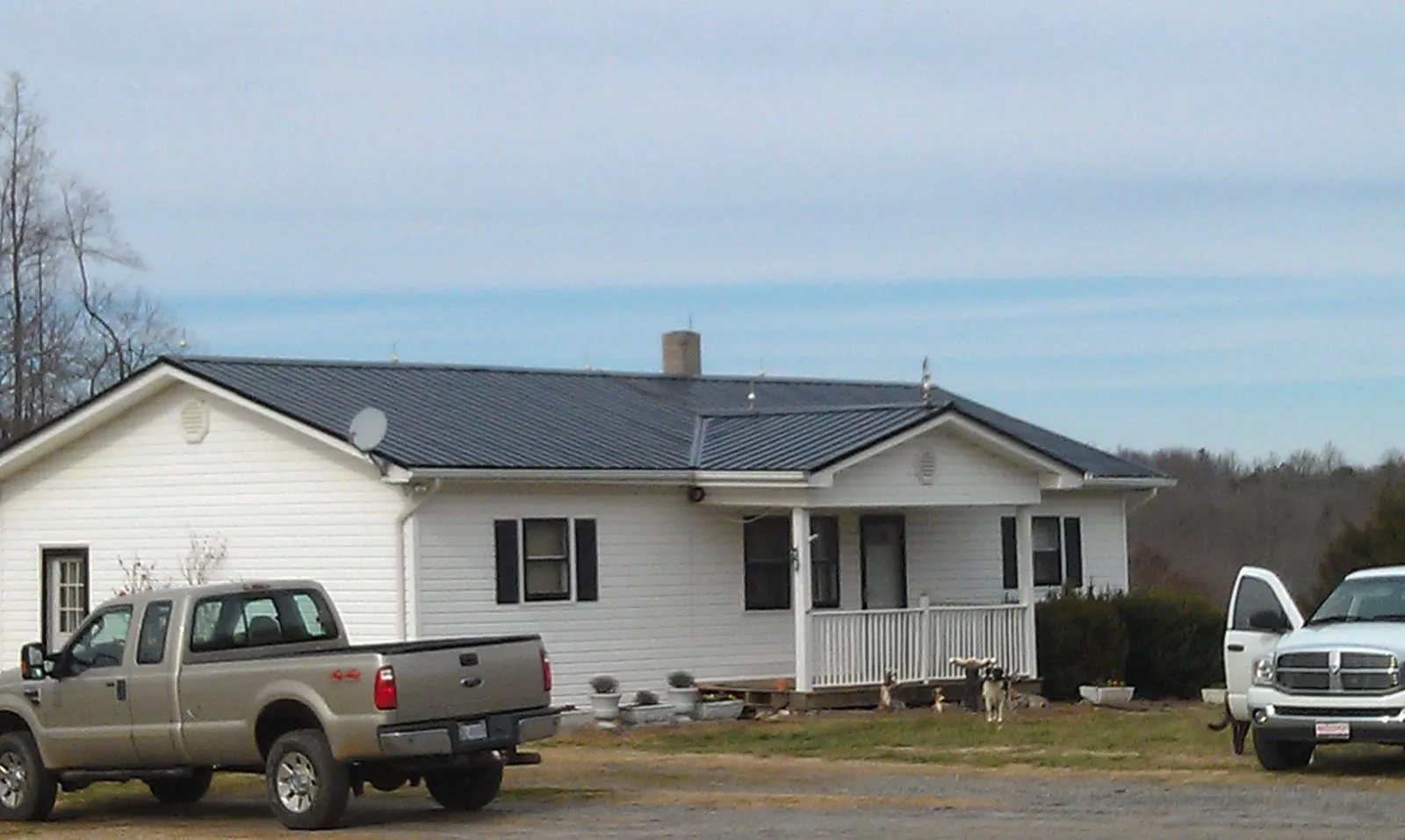 Finished dark metal roof on a white ranch home with work trucks parked in Cecil